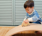Child playing with the Piccalio Surfer Balance Board and using it as a race course for play car. Available from www.tenlittle.com