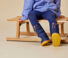 Kid sitting and wearing Ten Little Snow Boots in Navy and Pink. Available at www.tenlittle.com