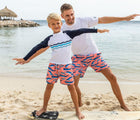 Child on the beach with a surfboard wearing the Snapper Rock One piece UPF 50+ Swim Shorts - Whales. Available from www.tenlittle.com
