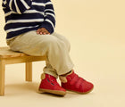 Child sitting wearing Ten Little Furry High Top - Lava Red. Available at www.tenlittle.com