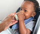 Parent holding Ezpz Tiny Bowl in Sage. Baby Drinking. Available at www.tenlittle.com