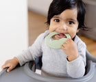 Child sitting in highchair using the mini development tool from ezpz Oral Development Tools in sage. Available from tenlittle.com