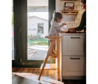 hild standing on All Circles Toddler Tower in natural in the kitchen. Available from tenlittle.com