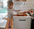 Child standing on All Circles Toddler Tower in natural in the kitchen. Available from tenlittle.com