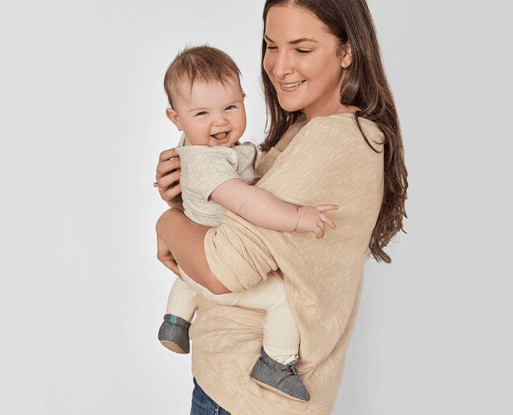 Mom carrying baby wearing Ten Little Everyday Baby Booties - Heather Gray. Available at www.tenlittle.com