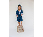 Girl Standing at the chair wearing Malabar Baby Hooded Muslin Robe - Mystical Night- Available at www.tenlittle.com