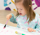 Girl painting in Bumkins Rainbow Long Sleeved Bib. Available from www.tenlittle.com.