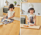 Girl playing in the kitchen and wearing Plan Toys Chef play set - Available at www.tenlittle.com