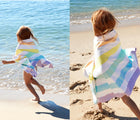 Girl wrapped in Dock & Bay Unicorn Wave Quick Dry Beach Towel on the beach. Available from www.tenlittle.com.
