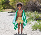 Boy wrapped in Dock & Bay Crocodile Quick Dry Beach Towel on the beach. Available from www.tenlittle.com.