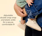 Parent holding child wearing Ten Little Sherpa Baby Booties with adjustable double-snap strap and elastic ankle for a secure, comfortable fit. Available at www.tenlittle.com