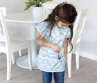 Child wearing the Bumkins Short-Sleeved Art Smock - Rainbows. Available from www.tenlittle.com