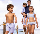 Boy at beach with family wearing Snapper Rock UPF 50+ Swim Shorts - Blue Stripes. Available at www.tenlittle.com