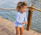 Girl at beach wearing Snapper Rock One Piece UPF 50+ Swimsuit - Blue Stripes. Available at www.tenlittle.com