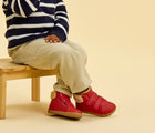Child sitting wearing Ten Little Furry High Top - Lava Red. Available at www.tenlittle.com
