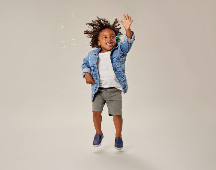 Child playing with bubbles wearing Ten Little Slip-On Sneakers - Navy Blue. Available at www.tenlittle.com