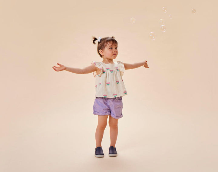 Child playing with bubbles wearing Ten Little Slip-On Sneakers - Navy Blue. Available at www.tenlittle.com