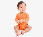 Baby sitting wearing Primary Baby One-Piece Rash Guard - Cantaloupe. Available at www.tenlittle.com