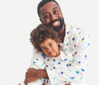 Adult with child wearing Primary Holiday PJ Set - Rainbow Village - Ivory Rainbow Winter Village. Available at www.tenlittle.com