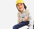 Child sitting wearing Primary Long Sleeve Button Down - Rainbow Flannel - Marshmallow / Rainbow Plaid. Available at www.tenlittle.com