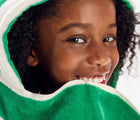 Child wearing Primary Hooded Towel in Green Apple Stripe. Available from www.tenlittle.com