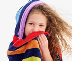 Child wearing Primary Hooded Towel in Navy Rainbow Stripe. Available from www.tenlittle.com