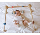 Baby on bed underneath PlanToys Wooden Play Gym in orchard. Available from tenlittle.com