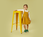 Girl Standing beside yellow chair wearing Ten Little Kids Everyday Original - Emerald Green - Available at www.tenlittle.com