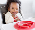 Baby in high chair holding Ezpz First food set - Mini Mat in coral. Available at www.tenlittle.com