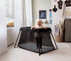 Child in playroom standing in BabyBjörn Travel Crib Light in black. Available fromten little.com