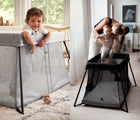 One view of child standing up in BabyBjörn Travel Crib Light in silver, and another view of adult putting baby inside BabyBjörn Travel Crib Light in black. Available fromten little.com