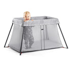 Child standing inside of BabyBjörn Travel Crib Light in silver. Available from tenlittle.com