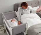 Bassinet from Béaba Air Complete Sleep System Bassinet-to-Crib next to adult laying in bed. Available from tenlittle.com