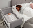 Baby in Béaba Convertible Air Bedside Sleeper Bassinet, next to adult laying in bed. Available from tenlittle.com