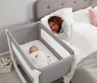 Baby in Béaba Convertible Air Bedside Sleeper Bassinet, next to adult laying in bed. Available from tenlittle.com