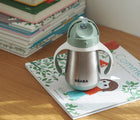 Beaba Stainless Steel Straw Sippy Cup on top of a book on a table. Available from tenlittle.com