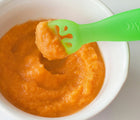 Green utensil from ChooMee Learning Utensil - Set of 2 being dipped inside bowl with puree inside of it. Available from tenlittle.com
