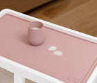 ezpz Tiny Placement in blush placed on highchair tray with cup on it. Available from tenlittle.com