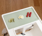 ezpz Tiny Placement in sage placed on highchair tray with food on it. Available from tenlittle.com