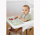 Child sitting in highchair eating from the ezpz Tiny Placement in sage. Available from tenlittle.com