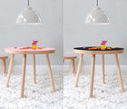 Two views of Nico & Yeye Round Craft Table in a playroom underneath hanging light - one view of table in pink & one view of table in black. Available from tenlittle.com