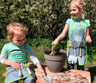 Two children using Small Foot Gardening Apron with Tools while playing outside. Available from tenlittle.com