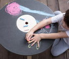 Child drawing with chalk on the PlanToys Round Chalkboard Table. Available from tenlittle.com