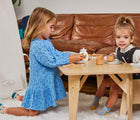 Two kids playing with Small Foot Wooden Tea Party Set at a table next to a couch. Available from tenlittle.com