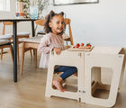 Girl sitting on Piccalio Convertible Kitchen Helper Tower in natural converted into table and eating food and smiling. Available from tenlittle.com