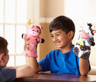 Child with pig hand puppet in one hand and cow hand puppet in other hand from Melissa & Doug Farm Friends Hand Puppets. Available from tenlittle.com