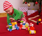 Child playing with Bigjigs Pull Along Train under a Christmas treee. Available from www.tenlittle.com.